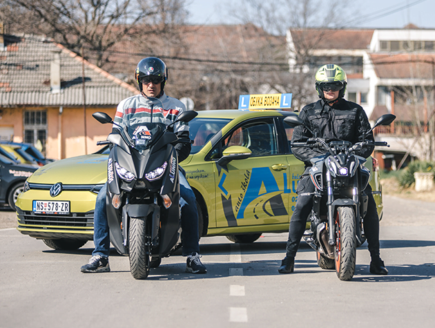 2 instruktora vožnje sede na motorima, a iza njih je parkiran automobil auto škole Alunno.