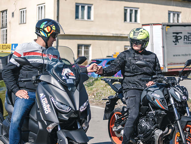 2 instruktora vožnje sede na motorima auto škole Alunno, na parkingu u Novom Sadu, i rukuju se.