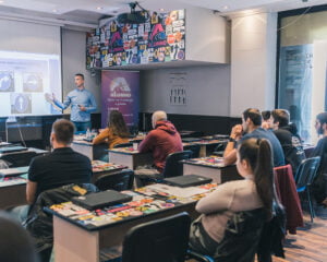 Predavač pokazuje kandidatima na tabli saobraćajne znakove za obavezno kretanje vozila.